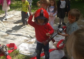 Zdjęcie przedstawia grupę dzieci, które poznają akcesoria strażaka potrzebne mu do wykonywania jego odważnej, odpowiedzialnej pracy